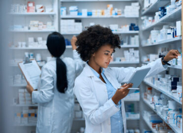 Shot of a young woman doing inventory in a pharmacy on a digital tablet with her colleague in the background